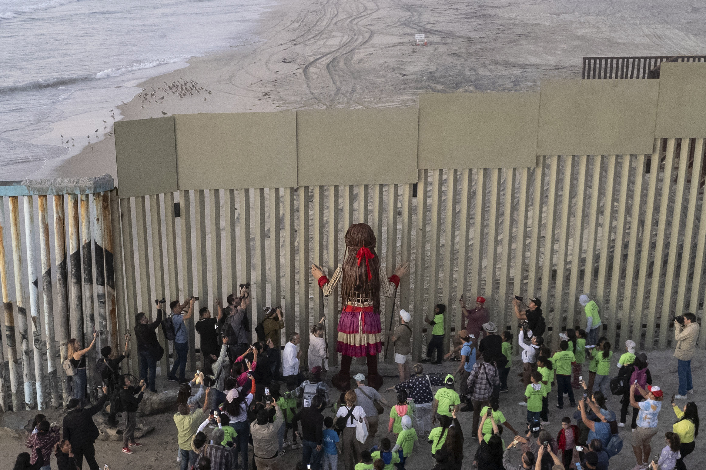 Little Amal, a 12-foot-tall puppet representing a ten-year-old Syrian refugee child, looks on through the US-Mexico border wall in Playas de Tijuana, Baja California state, Mexico on November 6, 2023. - Little Amal is visiting Tijuana within the framework of a journey across Mexico to raise awareness of the plight of refugees and migrants across the globe. (Photo by Guillermo Arias / AFP)