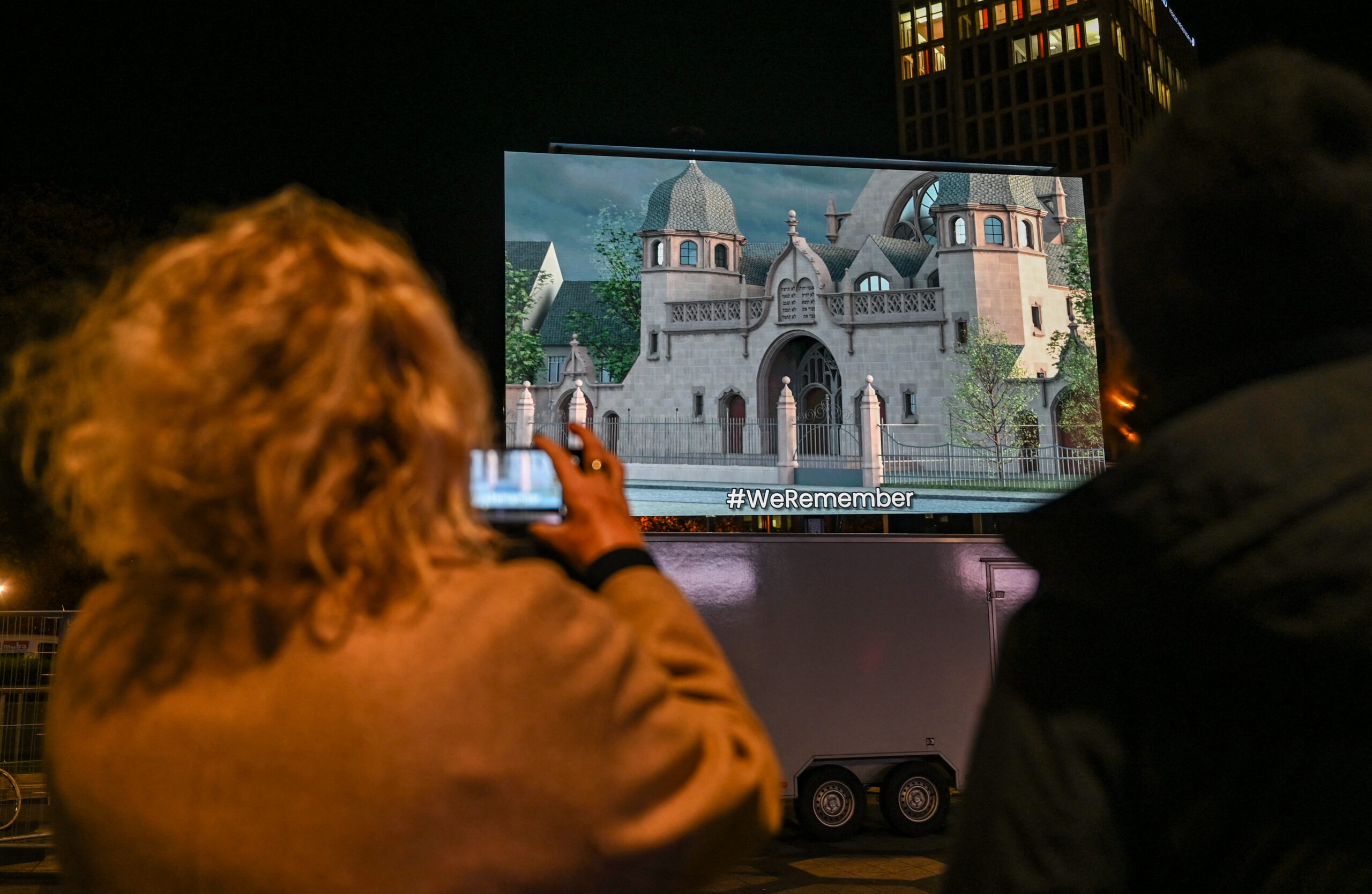 A woman takes a photo of a video installation showing a model of the former Dortmund synagogue during a rally organised by German parties in Dortmund, western Germany on November 9, 2023, to commemorate the 85th anniversary of the Night of Broken Glass (Kristallnacht) pogrom that began the Holocaust, and also in support of Israel and the hostages being held by Palestinian militant group Hamas. - On November 9-10, 1938, Nazi thugs murdered at least 90 Jews, torched 1,400 synagogues across Germany and Austria and destroyed Jewish-owned shops and businesses. Thousands of civilians, both Palestinians and Israelis, have died since October 7, 2023, after Palestinian Hamas militants based in the Gaza Strip entered southern Israel in an unprecedented attack triggering a war declared by Israel on Hamas with retaliatory bombings on Gaza. (Photo by Ina FASSBENDER / AFP)
